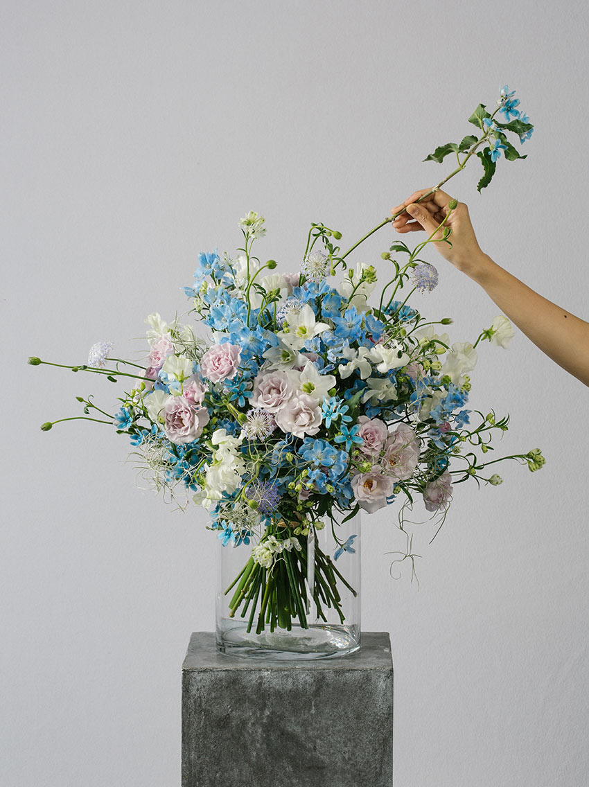 Florist arranging a luxury flower bouquet of eucharis, delphinium and sweet peas. Featuring bespoke bouquet 27.